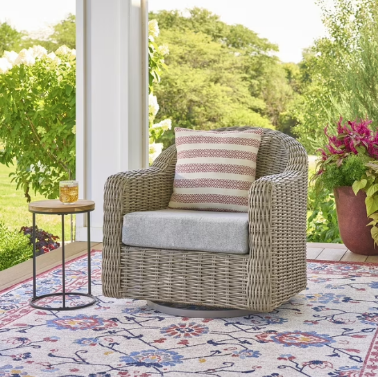 Outdoor wicker swivel chair with gray cushion and striped pillow.